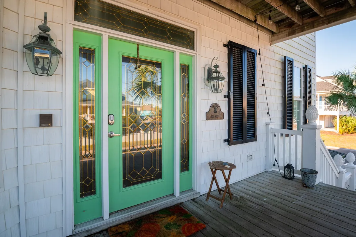 A vibrant exterior shot featuring a green door, stylized lanterns, a decorative welcome plaque, and a colorful doormat. The porch area looks inviting, suggesting a comfortable and welcoming entryway for all members of the family, pets included.