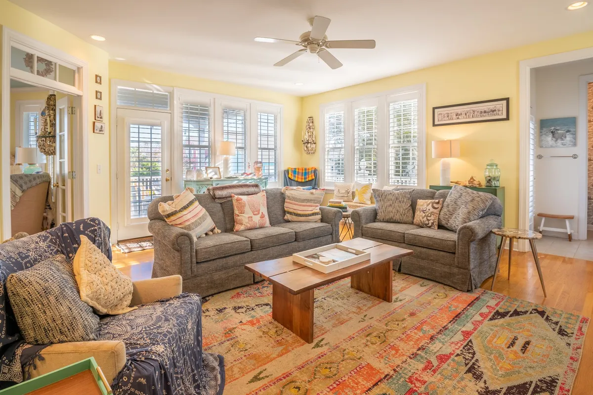 A comfortable living room featuring plush sofas, a coffee table, and expansive windows that flood the space with light. The room is set up for both relaxation and conversation, creating an ideal spot for movie nights, board games, or unwinding after a day at the beach.