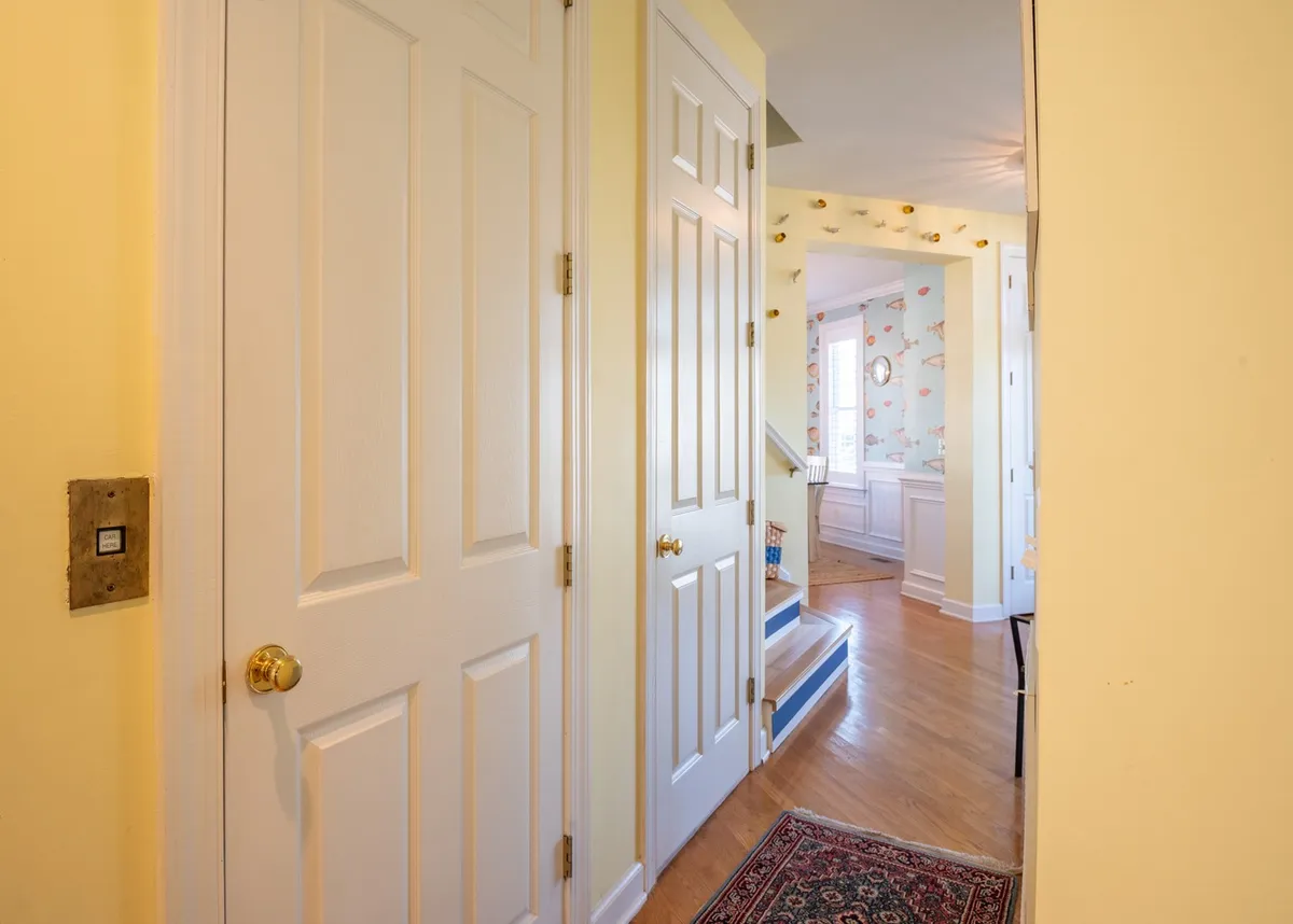 This image captures the home's inviting entryway, featuring yellow walls, wooden stairs, a decorative rug, and multiple open doorways. The scene evokes a sense of transition from inside to out, suggesting a welcoming starting point for daily adventures.