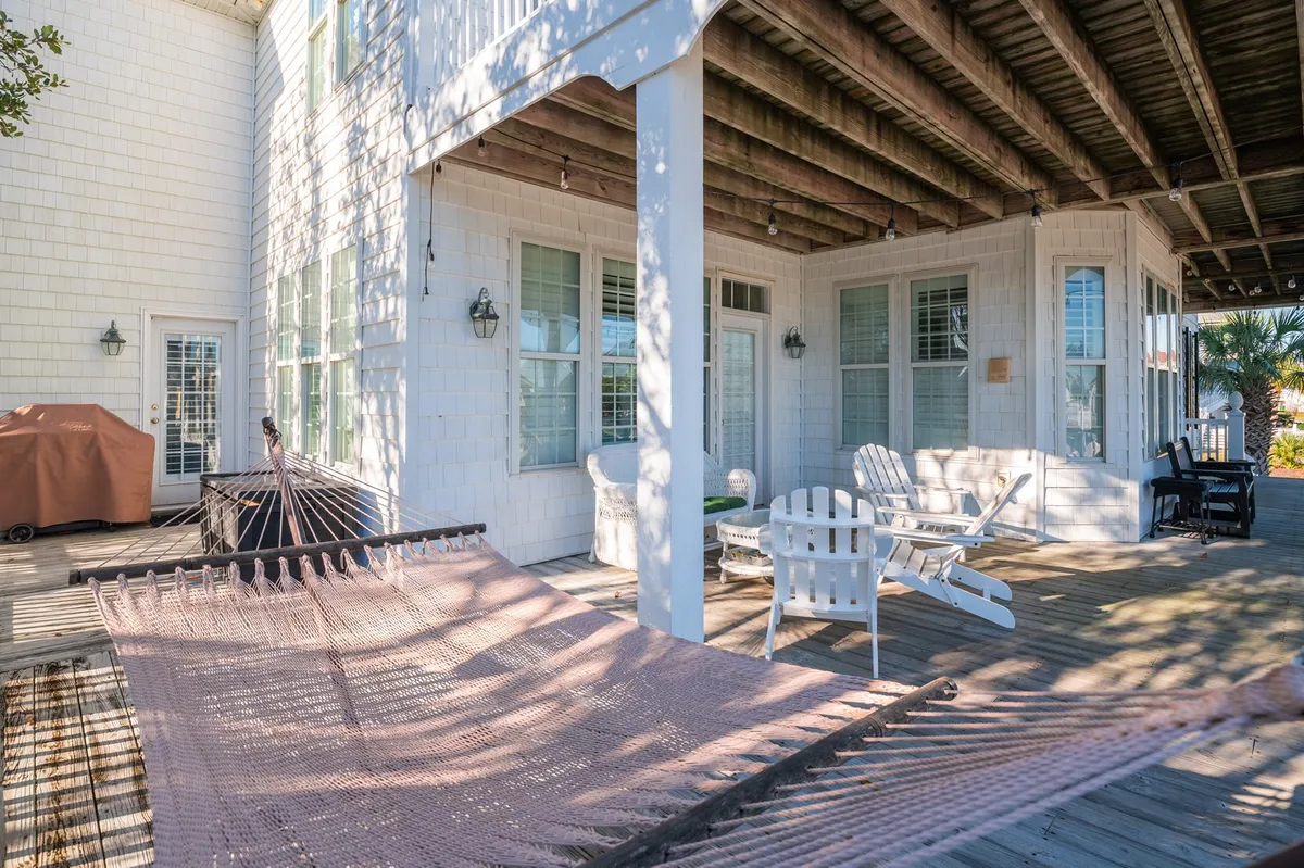 An outdoor deck adorned with a hammock and white chairs, surrounded by palm trees. The space is inviting and set up for both relaxation and group socializing, offering an ideal setting for al fresco dining or evening conversations under the stars.