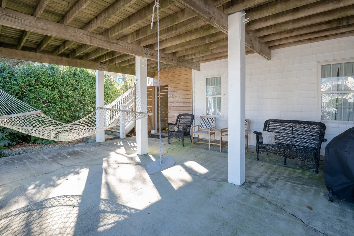 A laid-back, shaded patio featuring a hammock and seating area under wooden beams. The scene suggests relaxation, casual conversation, and outdoor enjoyment—perfect for lazy afternoons or unwinding after play.