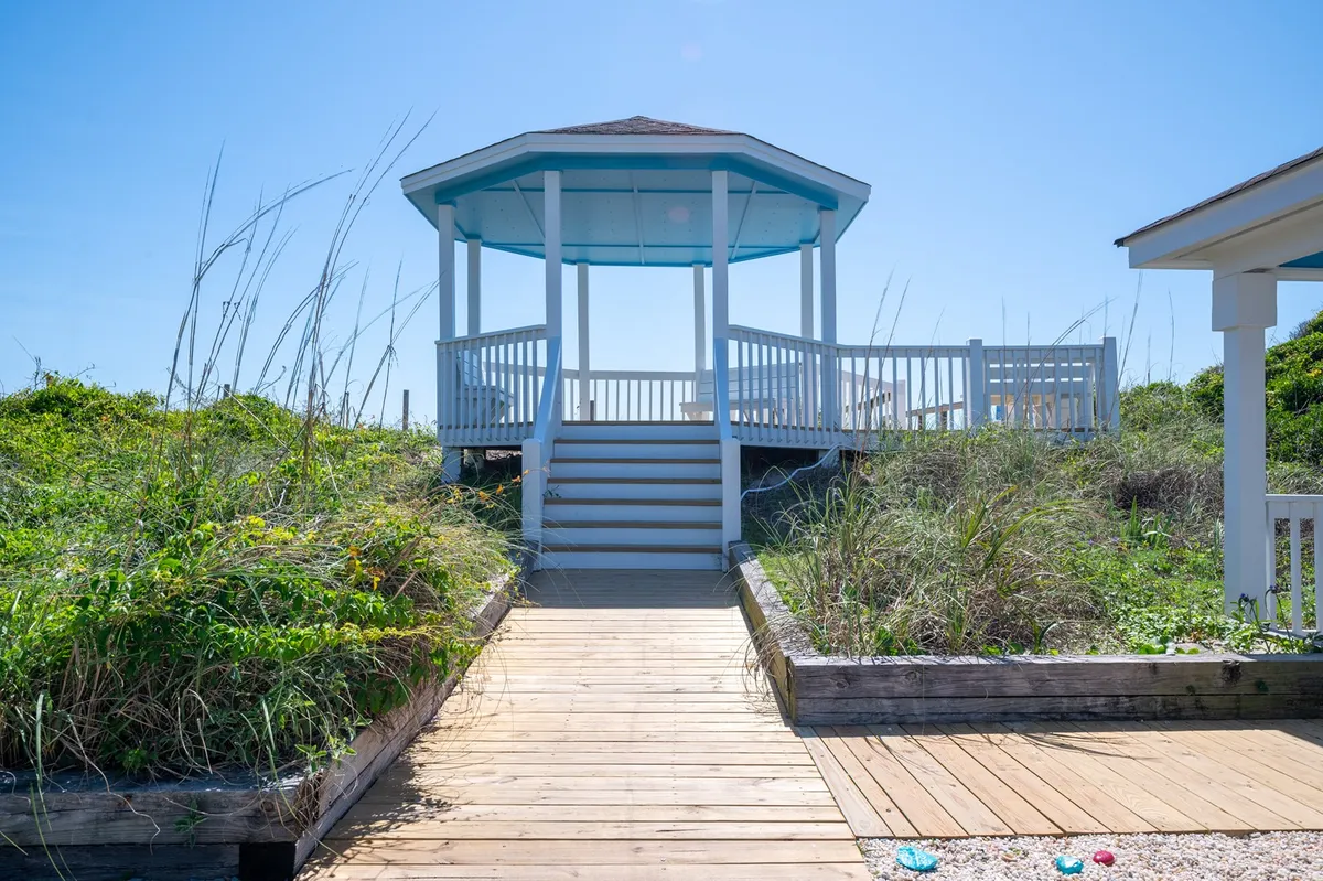 This image features a charming gazebo connected by a wooden walkway and surrounded by lush greenery. The peaceful outdoor space is suitable for group relaxation, casual gatherings, or celebrating special moments in nature.