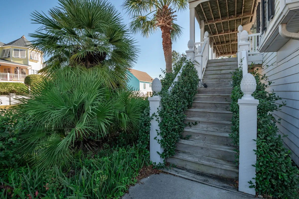 A welcoming exterior view with a wooden staircase flanked by palm trees and vibrant greenery, inviting guests to relax outdoors. The scene evokes the feeling of an inviting, tropical escape ideal for reunions and leisure.